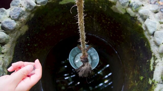 Moneda cayendo a pozo de los deseos hecho de piedra, con cubeta y lazo para sacar agua potable.