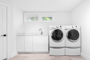 A laundry room with white cabinets and stainless steel faucet, white appliances, and brown tile...