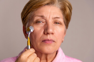 elderly woman granny portrait using derma roller on face anti wrinkle aging procedures. isolated...