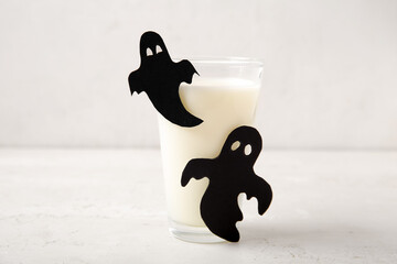 Glass of milk and ghosts made of paper for Halloween on light background, closeup