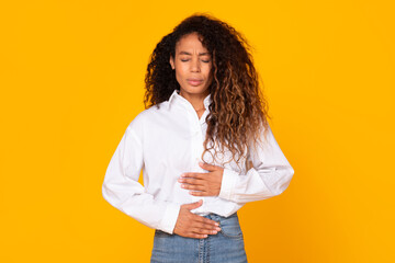 Black young woman touching stomach suffering from stomachache, yellow background