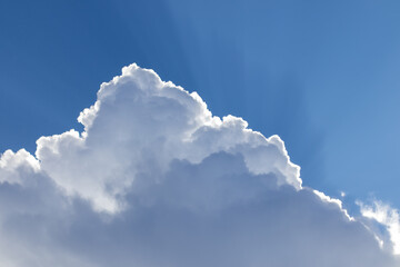Cumulus cloud with sunbeams radiating against a bright blue sky.