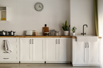 White counters with cooking pots, utensils and sink in modern kitchen