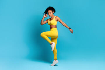 African fitness lady performing cardio workout jumping over blue background - obrazy, fototapety, plakaty
