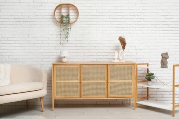 Modern light wooden chest of drawers with shelving unit and couch near white brick wall in room