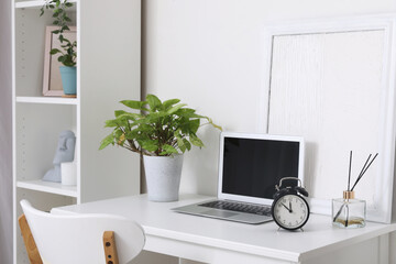 Modern laptop and alarm clock on table in room