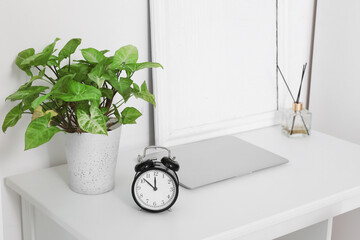White desk with alarm clock, laptop and houseplant, closeup