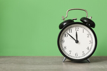 Alarm clock on table near green wall, closeup