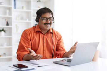 Smiling mature indian man using laptop and headset