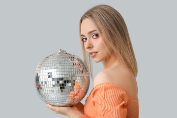 Beautiful young woman with disco ball on grey background