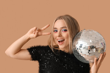Naklejka premium Beautiful young woman with disco ball showing victory gesture on brown background