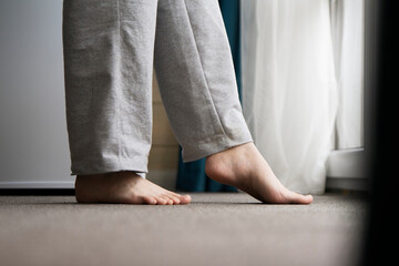 A close-up view shows bare feet standing on a carpeted floor, likely indicating the warmth from a heating system in a residential setting.