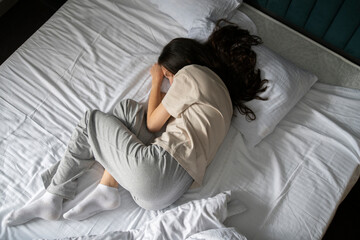 A woman is captured taking a nap, curled up in a bad wrong on a white-sheeted bed, suggesting a...