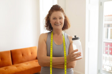 Confident senior woman wearing tape measure and holding water bottle