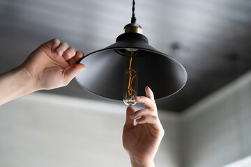 A man is captured in the act of changing a light bulb in a hanging ceiling light fixture, with...