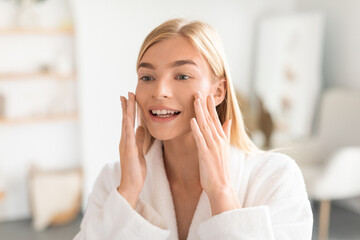 Joyful woman with blonde hair touching soft skin in bathroom