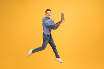 Fototapeta na wymiar Happy teen boy with laptop computer jumping up over yellow background