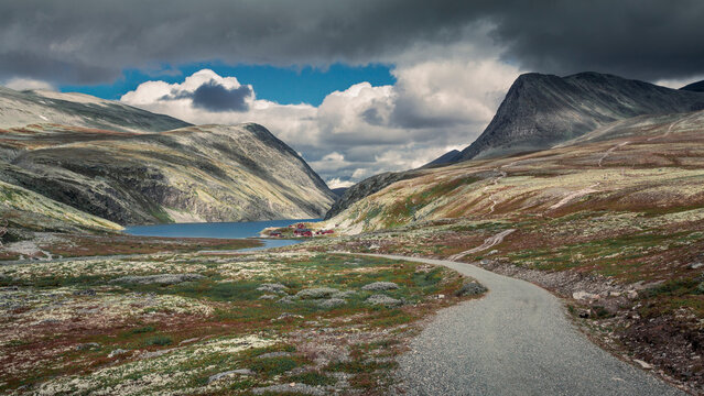 Rondane national park with footpath leading to lake Rondvassbu and hut, framed with mountains, cloudy dramatic sky, Norway.