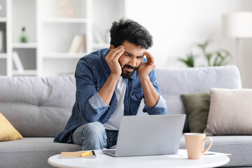 Stressed indian man having headache while working on laptop at home