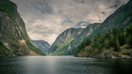 Moody fjord with mountains and waterfall of Aurlandsfjord at Gudvangen in Norway, dark clouds in...