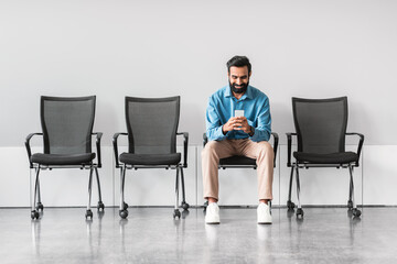 Indian man using smartphone while sitting in empty waiting area - Powered by Adobe