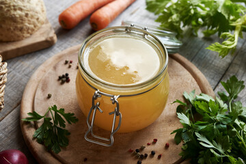 Bone broth in a glass jar on a table, with vegetables in the background