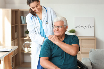Senior man in wheelchair holding nurse's hand at home