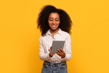 Smiling black woman using tablet, isolated on yellow background