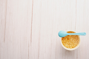 Obraz na płótnie Canvas Overhead view of a bowl of instant pasta soup with a spoon light blue on white background. Lunch. Fast food concept