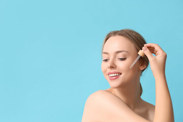 Beautiful young woman with cosmetic oil on blue background