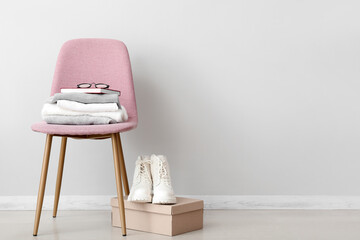 Stack of folded sweaters with book on pink chair and boots near white wall