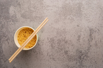 Overhead view of a bowl of instant pasta soup with a pair of chopstickson a light gray background. Lunch. Fast food concept