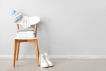 Stack of folded sweaters with hat on chair and boots near white wall