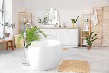 Interior of light room with white bathtub and counters