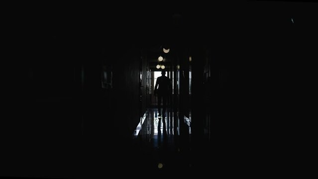 Unrecognizable image of the groom in a dark corridor. Silhouette of a man walking in a hotel corridor. The groom walks towards the bride along the corridor.