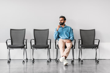 Pensive indian man in office with empty chairs, contemplating