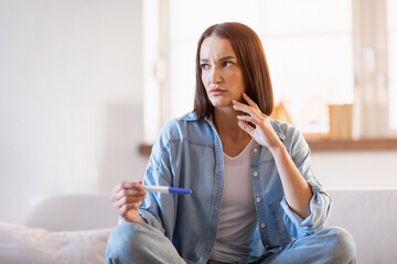 Thoughtful lady holds pregnancy test making decision sitting at home