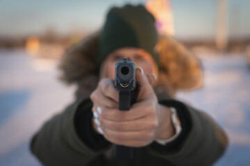 A young girl takes aim with a 9mm tactical pistol outdoors in winter. Soft focus photo.