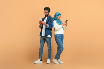 Modern arab muslim couple with their smartphones standing over beige background