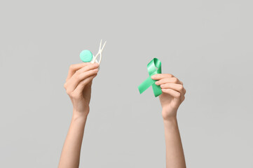 Female hands with green ribbon, container for contact lenses and tweezers on grey background....