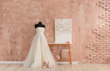 Mannequin with wedding dress, glasses of wine and engagement ring on table near beige wall. Valentine's Day celebration