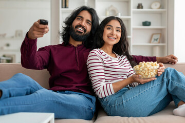 Relaxed millennial indian man and woman watching TV at home