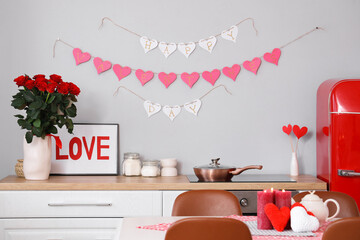 Interior of festive kitchen with paper heart garland and bouquet of roses on counter. Valentine's...