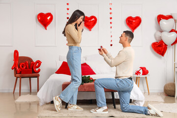 Young man proposing to his girlfriend in bedroom. Valentine's Day celebration
