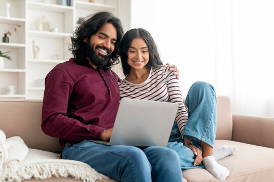 Positive young indian couple watching movie on laptop at home