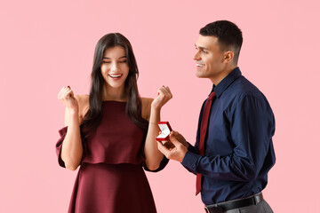 Young man proposing to his girlfriend on pink background. Valentine's Day celebration