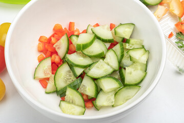 Bowl with pieces of sweet pepper and cucumber for preparing salad.
