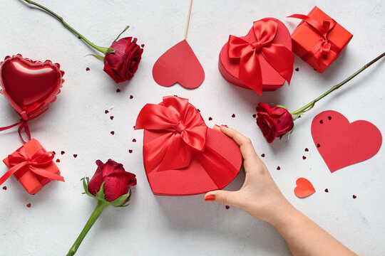 Female hand with red manicure, gift box and decor on white grunge background. Valentine's Day celebration