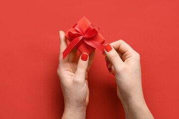 Female hands with red manicure and gift box on color background. Valentine's Day celebration