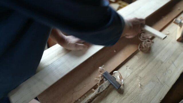 A thin wooden board is being cut into thinner pieces using special tools. Nearby, a chip, hammer, and other objects can be seen.